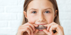 Attractive little girl stands on white background. Dental simulator for teeth alignment . The child has mouth guards on his teeth